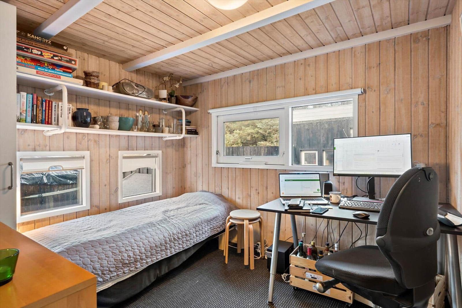 A bedroom with desk, bed, and windows on the walls.