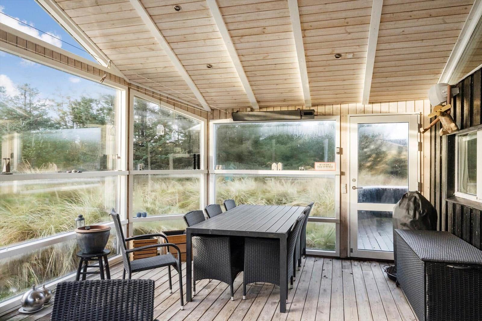 Patio with table and chairs, large windows and wooden ceiling.