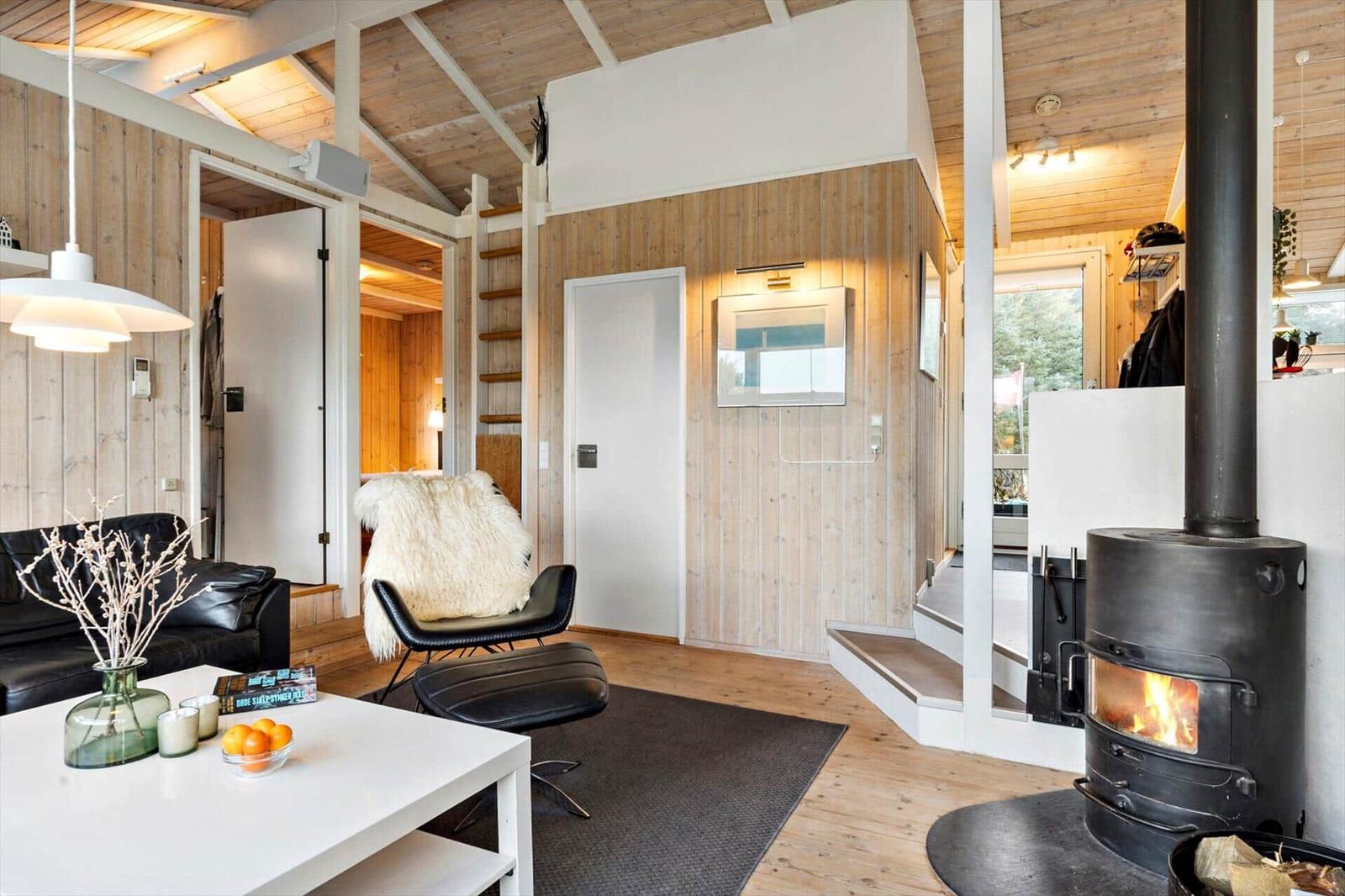 Living room with fireplace, sofa, and chair. Wooden walls and floor. Door to bedroom.