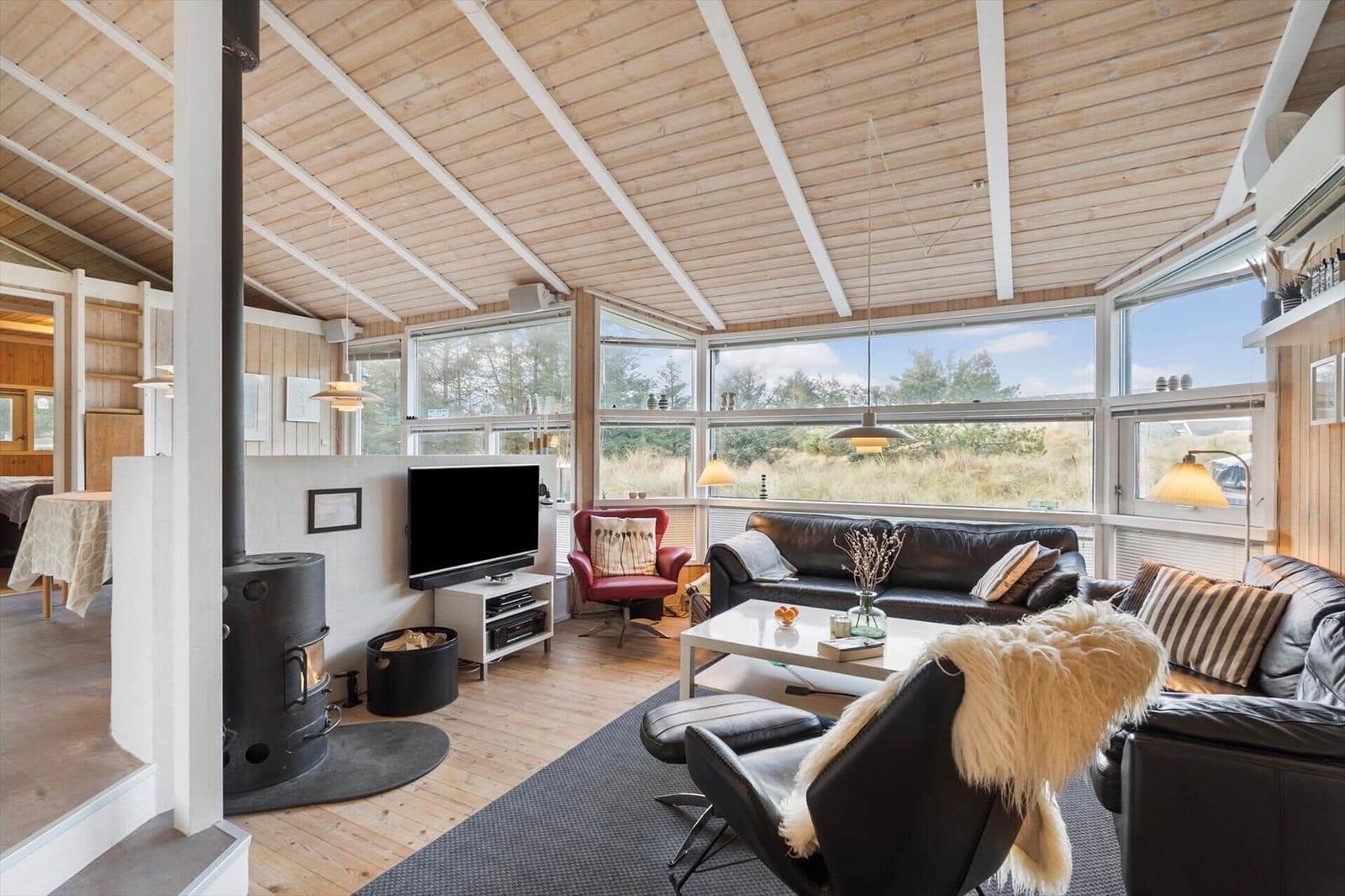 Living room with wooden ceiling, large windows, and black leather furniture.