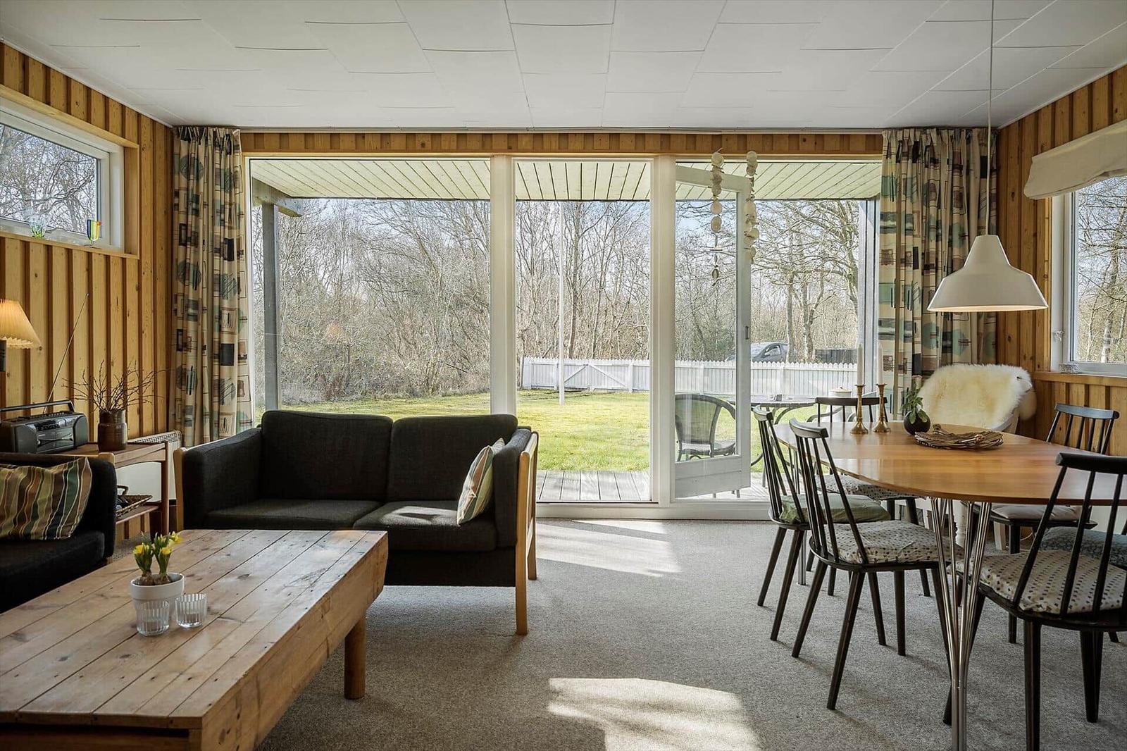 Living and dining area with wooden walls, sofa, table, and view of the garden.