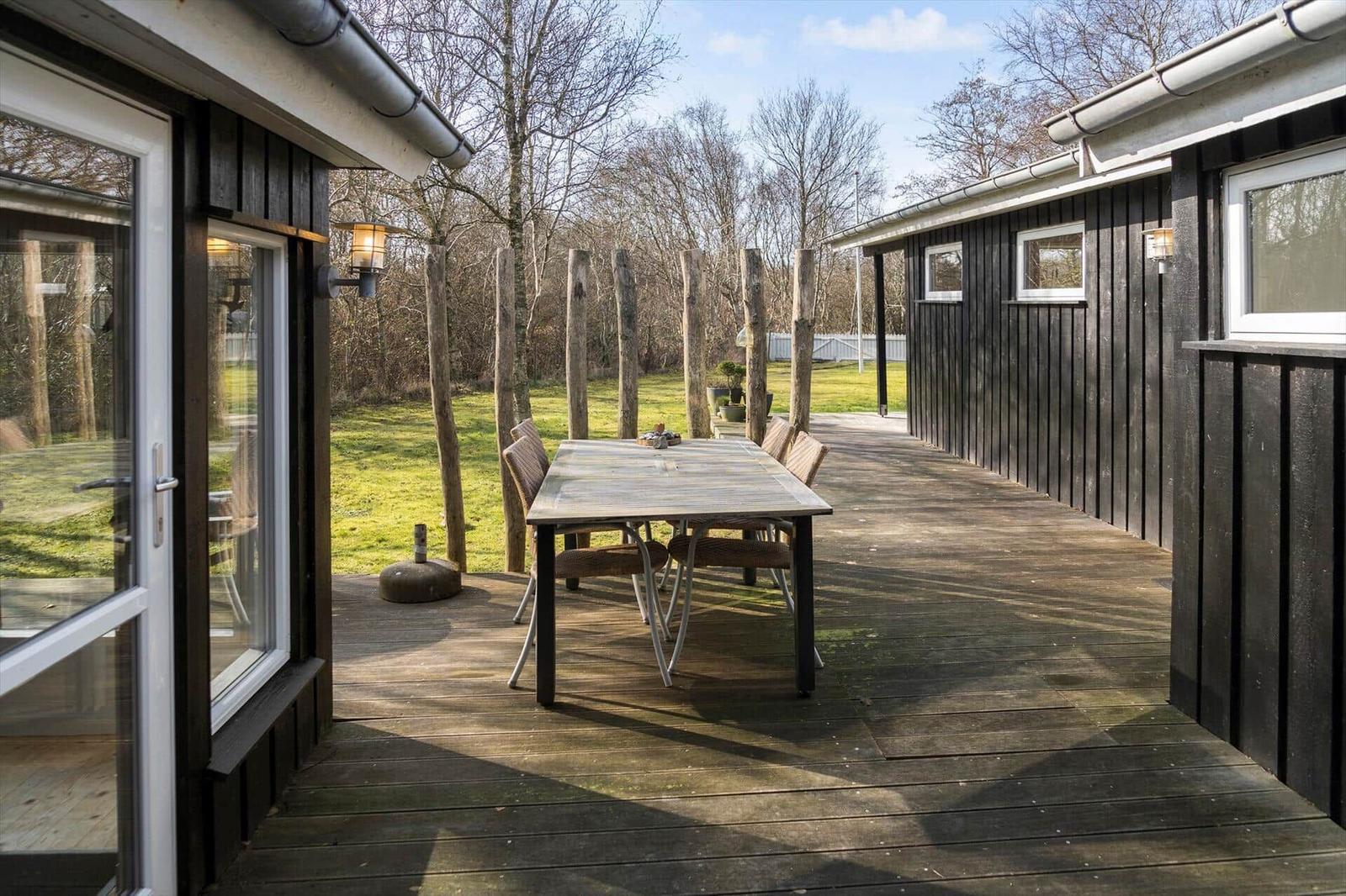 Deck with table and chairs, surrounded by forest and wooden walls.