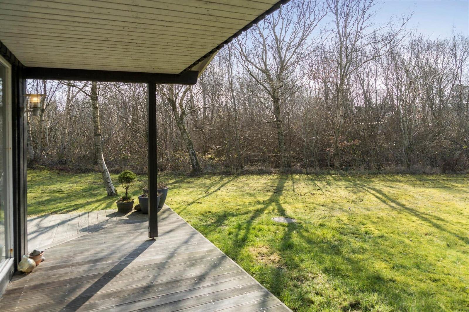 Deck with wooden roof and view of green lawn and trees.
