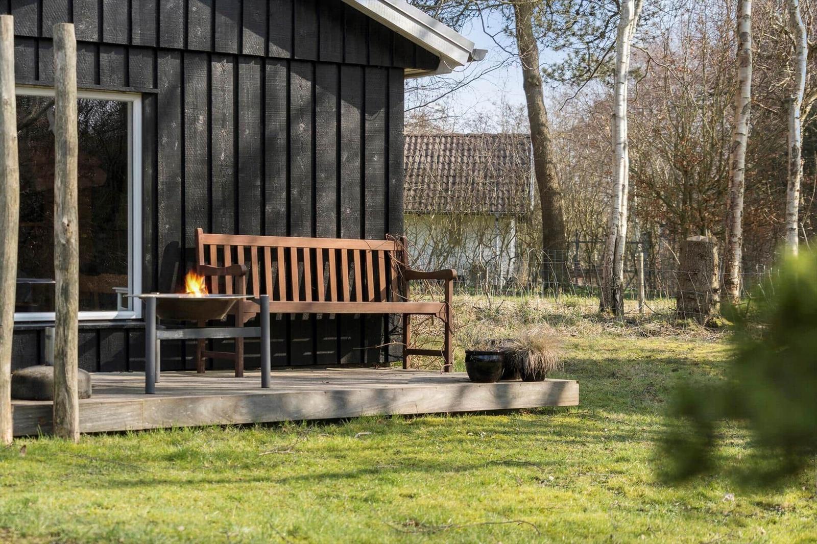 Wooden terrace with bench and fire pit in front of a dark wood house.