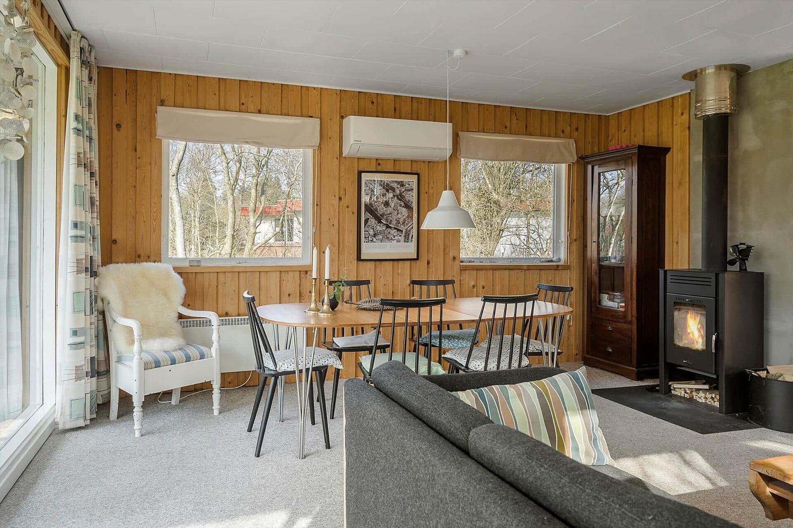 Living room with dining table, sofa, and wood stove. Wooden walls and large windows.