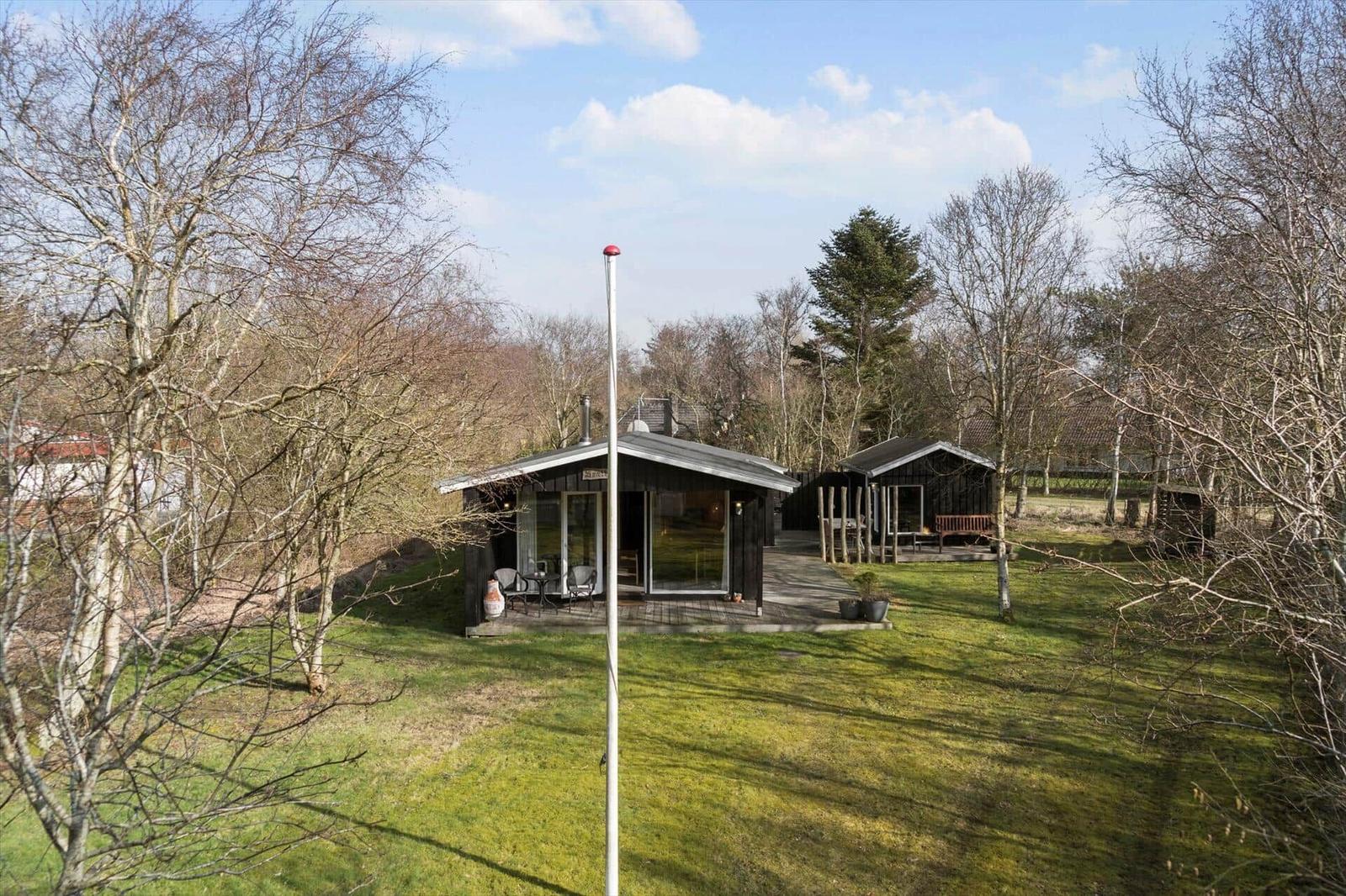 Two wooden houses with terraces stand in a green garden surrounded by trees.