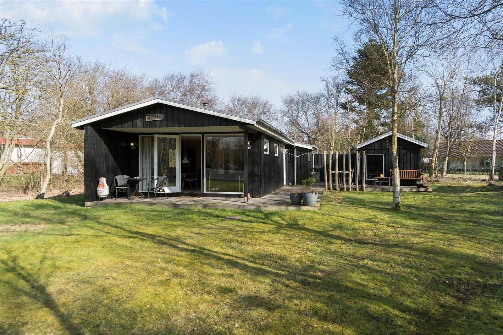 Black wooden cabin with terrace and garden. Attached building with fire pit.