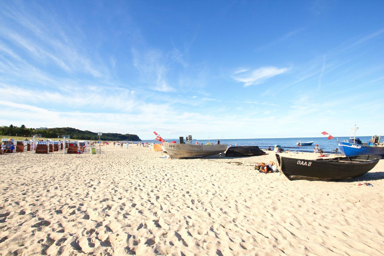 Strand mit Booten und Strandkörben unter blauem Himmel.