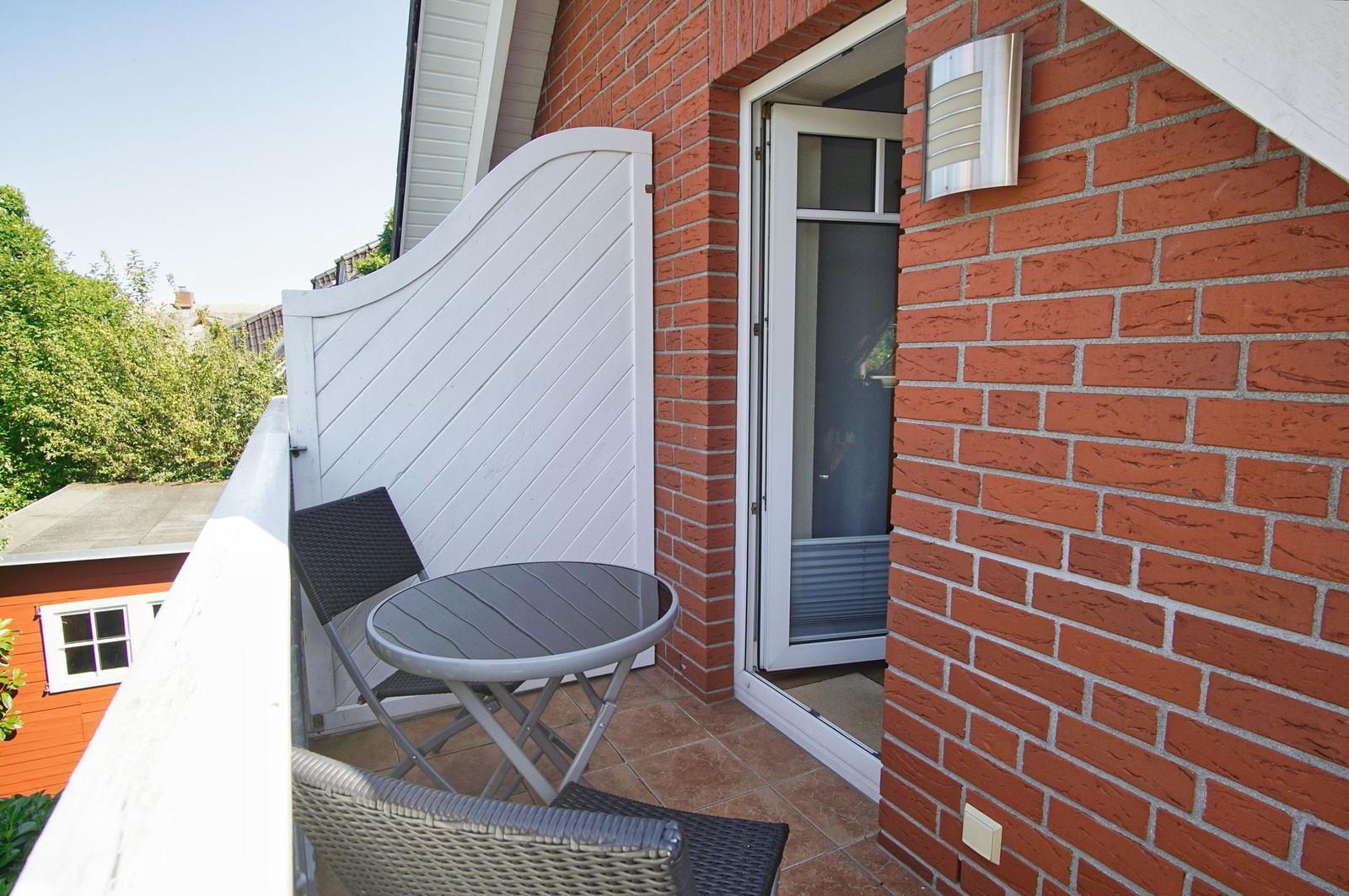 Terrasse mit Tisch und Stühlen neben rotem Backsteinhaus.