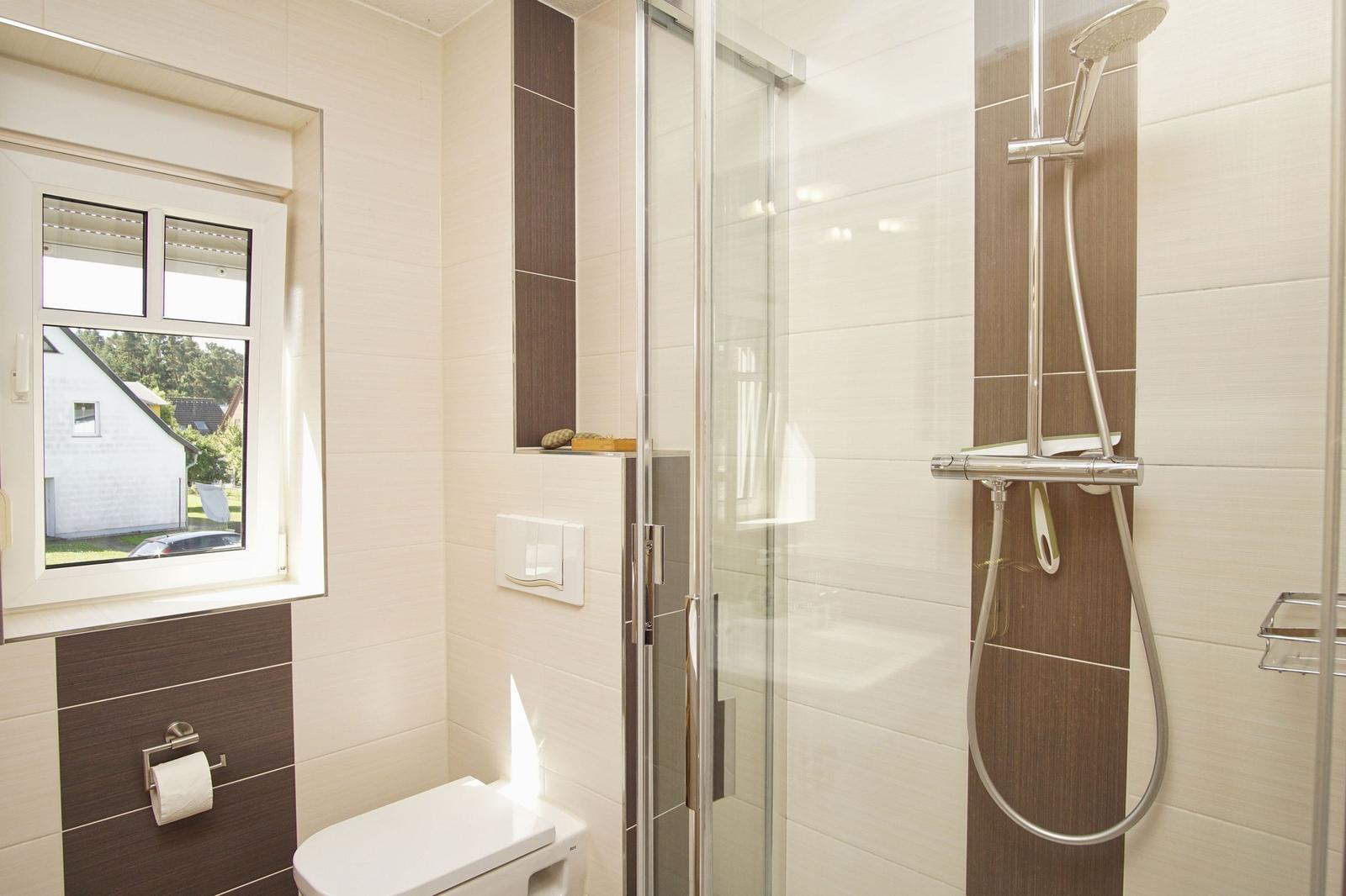 Bad mit Dusche, Toilette und Fenster. Fliesen in Beige und Braun.