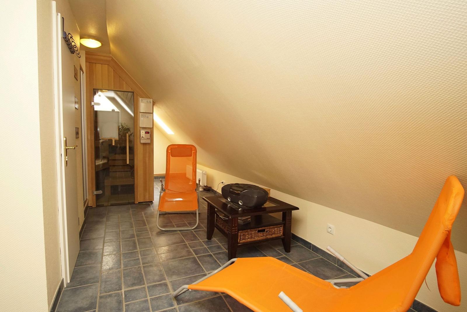 Zimmer mit zwei orangefarbenen Liegestühlen und einem Holztisch.