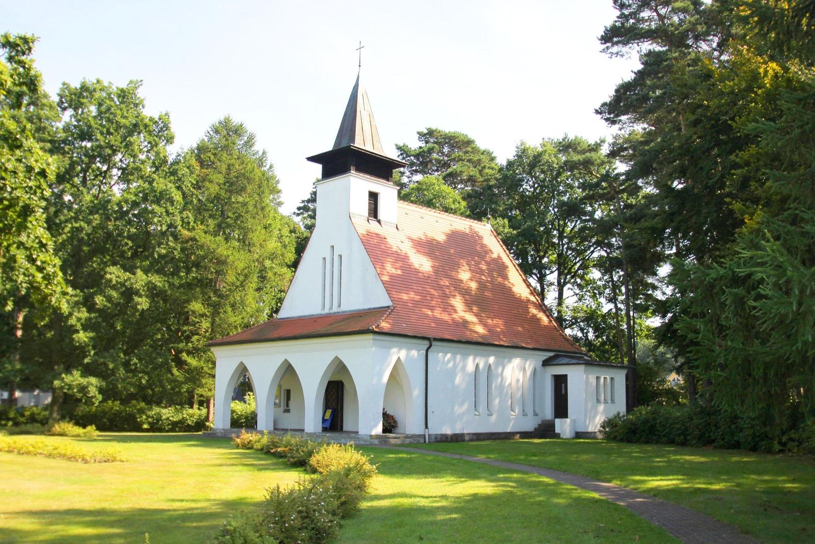 Weiße Kirche mit rotem Dach und spitzen Turm in grüner Umgebung.