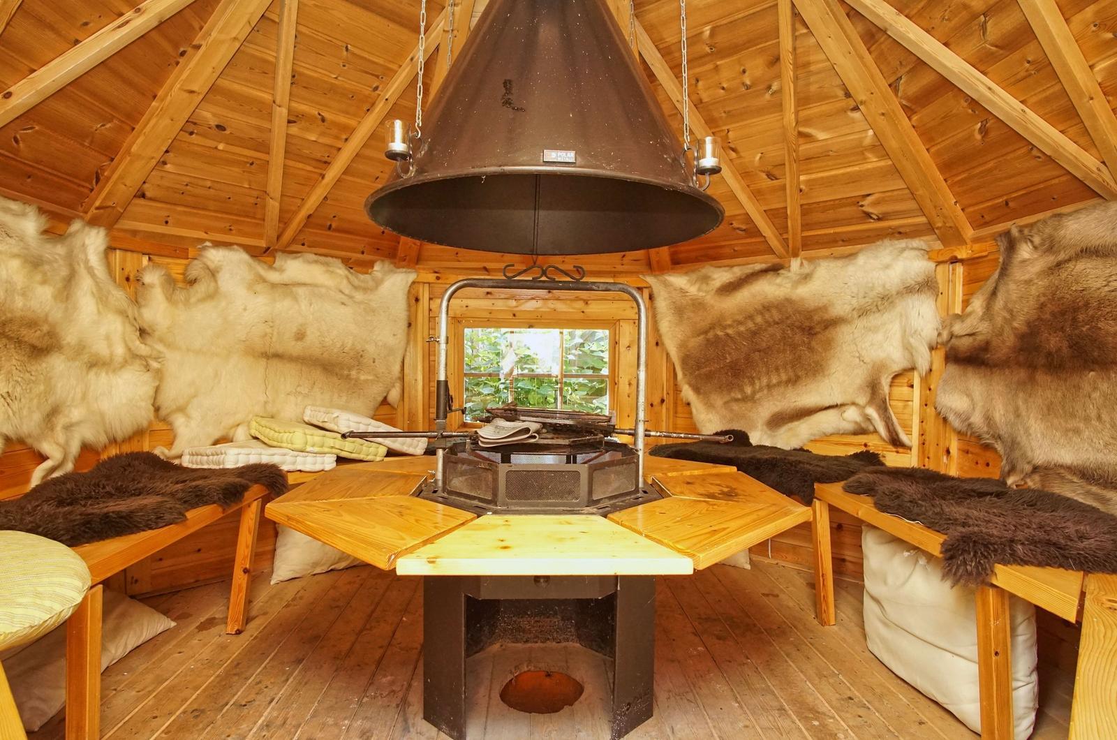 Holzvertäfelte Hütte mit Fellwand, zentraler Feuerkessel und Sitzbänken.