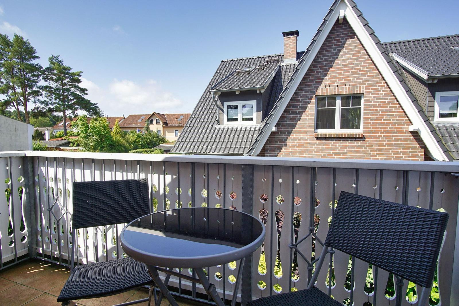 Terrasse mit Tisch und zwei Stühlen, Blick auf ein Haus mit Ziegelfassade und Dachgauben.