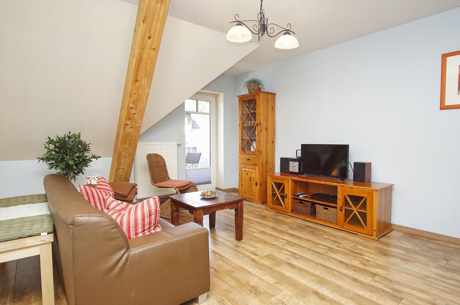 Wohnzimmer mit Sofa, Holzmöbeln und TV. Holzdecke und Fenster sichtbar.