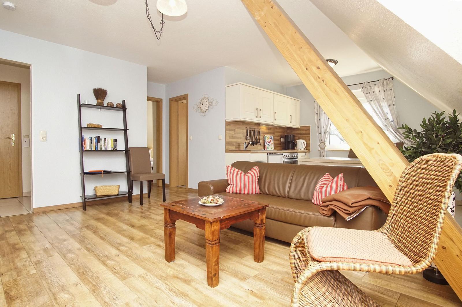 Wohn- und Küchenbereich mit Sofa, Tisch und Holzboden unter Dachschräge.