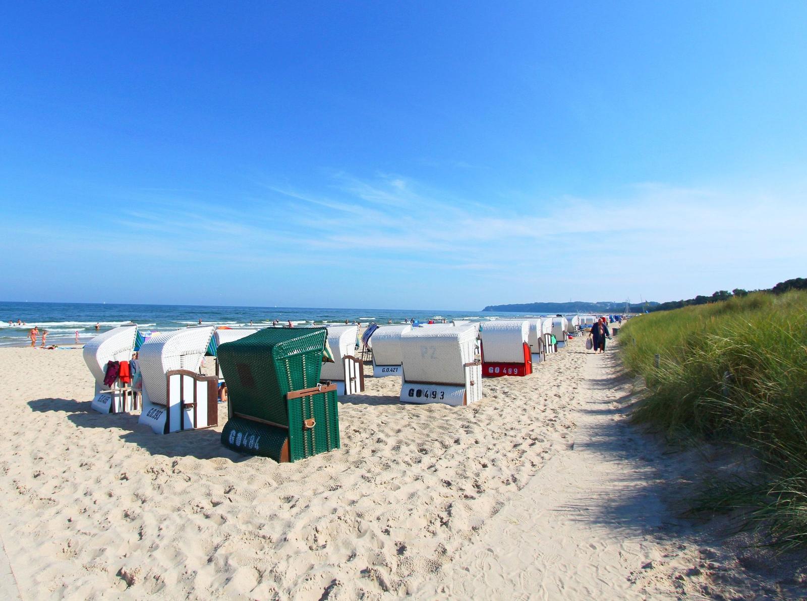Strand mit Liegestühlen und sandigem Pfad zur See.