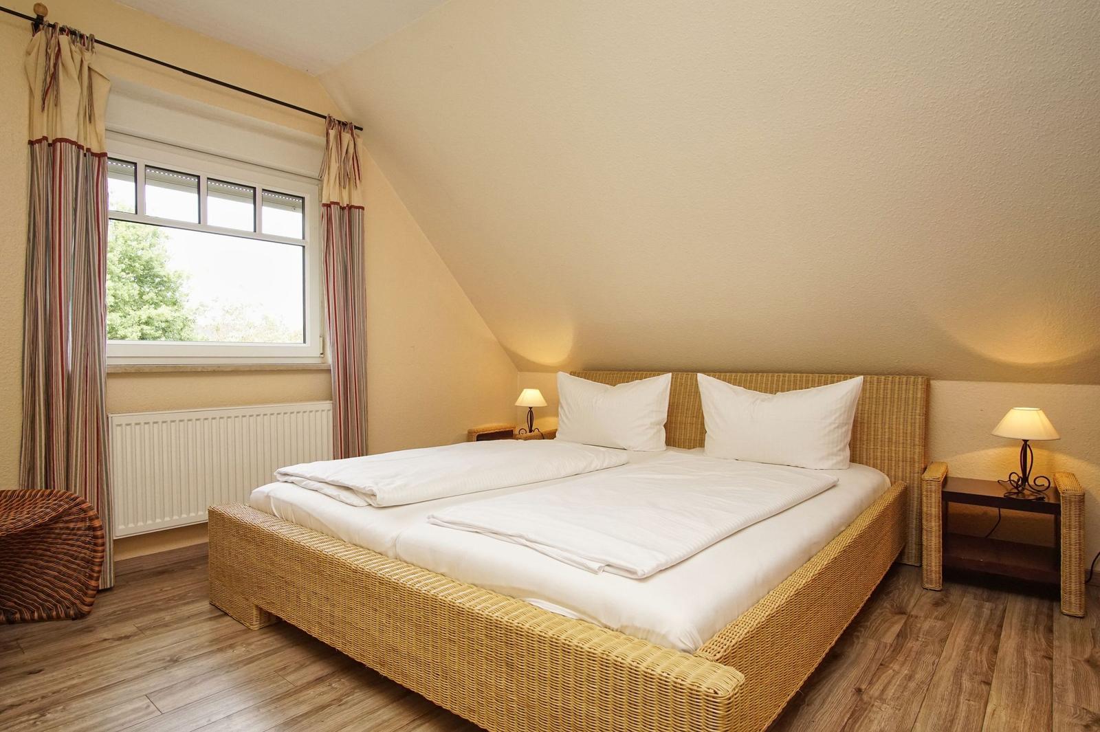 Schlafzimmer mit Doppelbett, Fenster und Nachttischen.