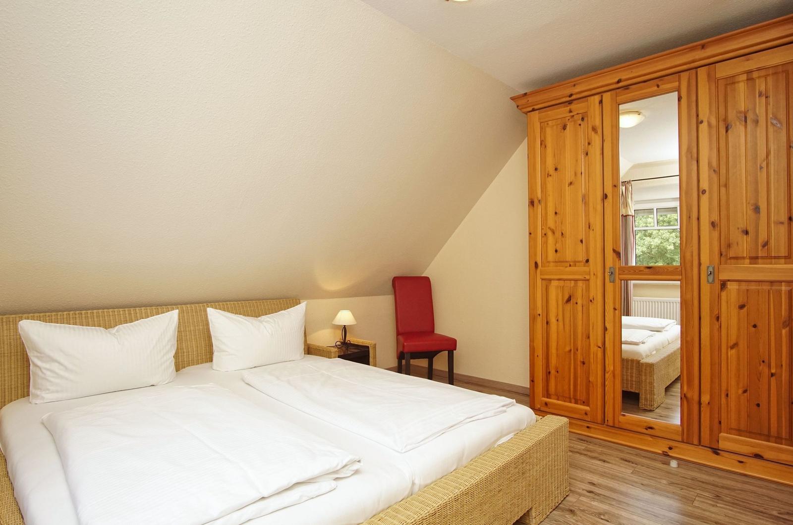 Schlafzimmer mit Doppelbett, Holzschrank und roter Sitzgelegenheit.