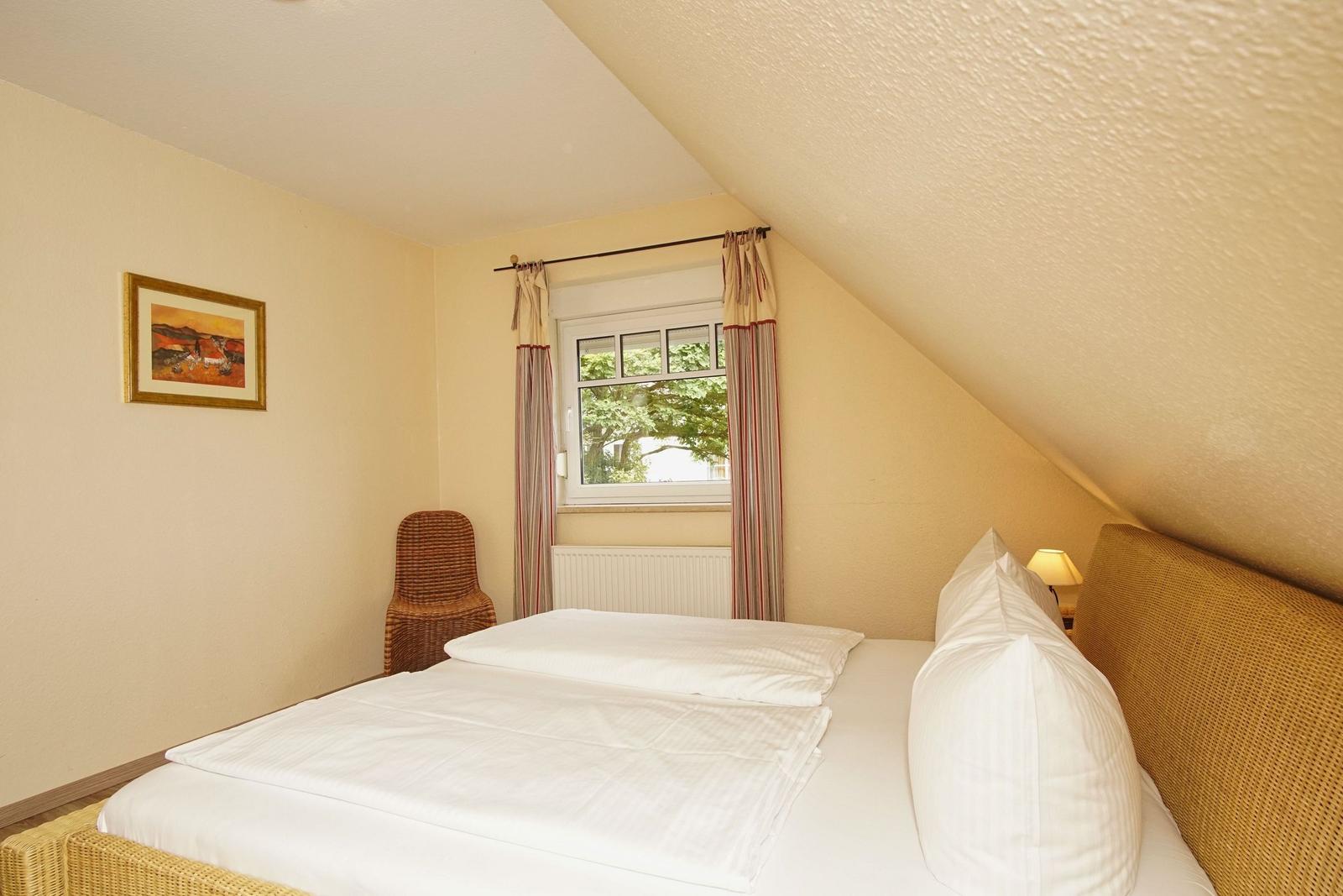 Schlafzimmer mit Dachschräge, Bett, Fenster und Stuhl.