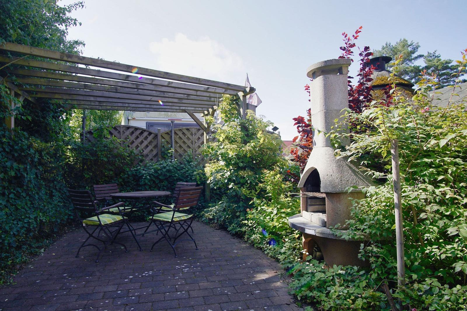 Garten mit Sitzgruppe, Pergola und Steinbackofen umgeben von Pflanzen.