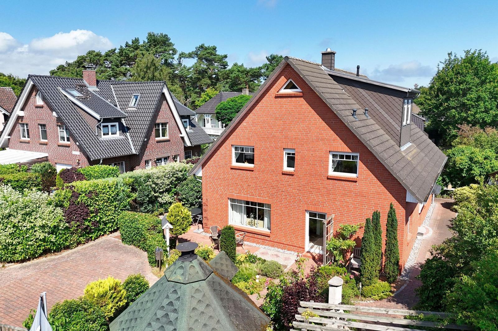 Rotes Backsteingebäude mit Garten und Terrasse. Umgeben von Bäumen und Nachbarhäusern.