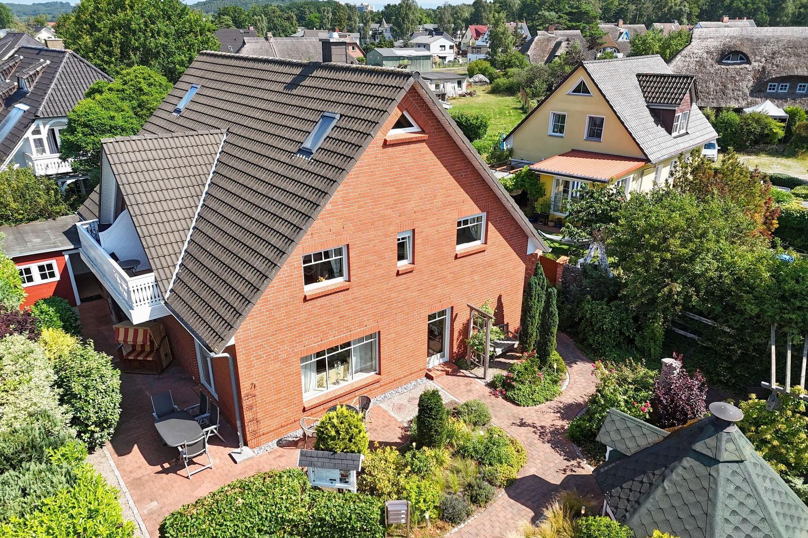 Rotes Backsteingebäude mit Balkon und Garten. Umgeben von Grün und Nachbarhäusern.
