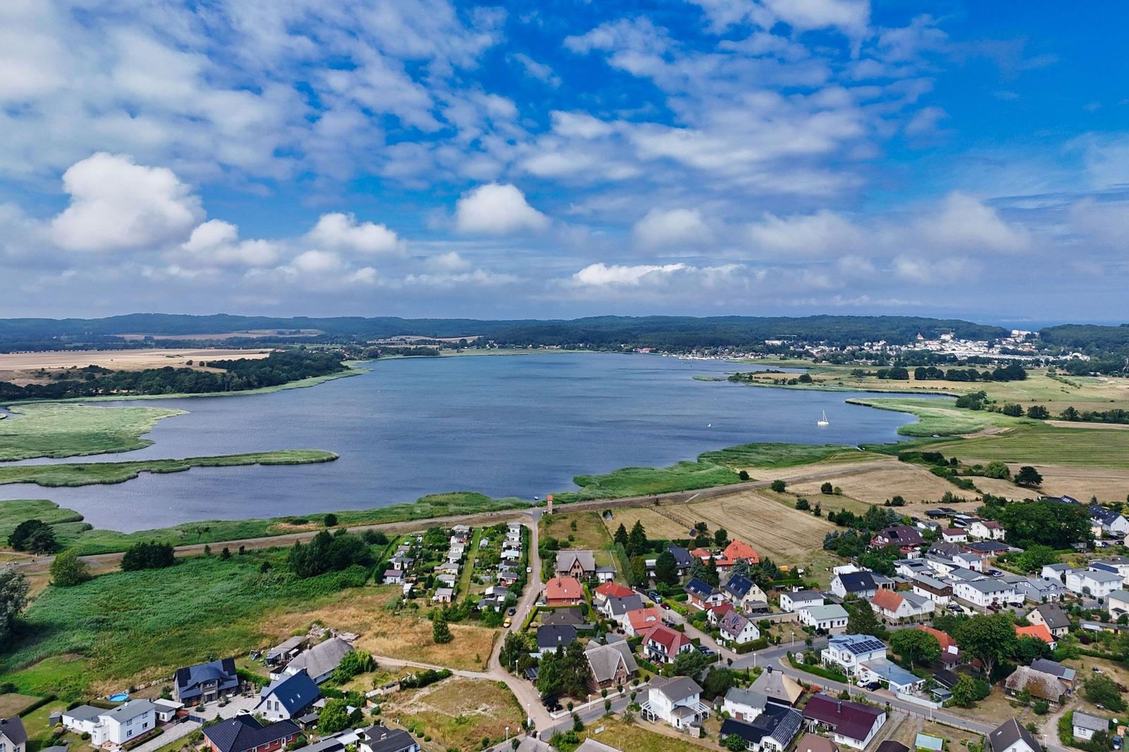 Aerial view of a lake with surrounding residential areas and green fields under a partly cloudy sky.