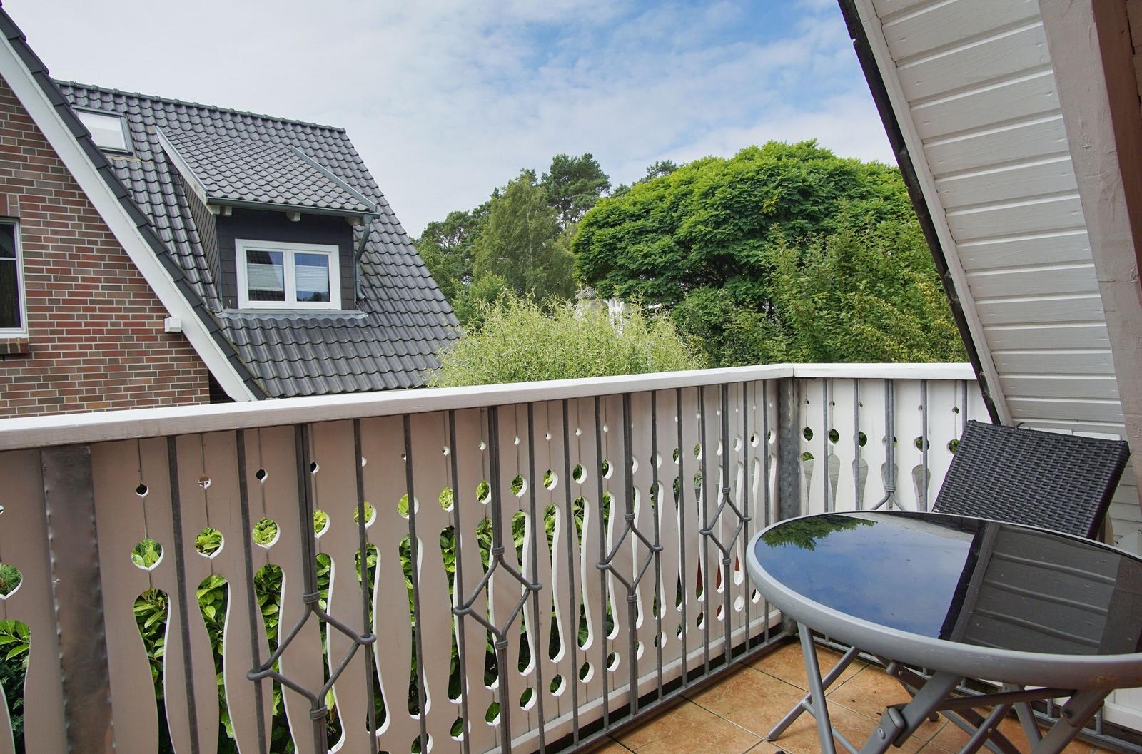 Terrasse mit Tisch und Stuhl, Blick auf grüne Bäume und benachbarte Häuser.