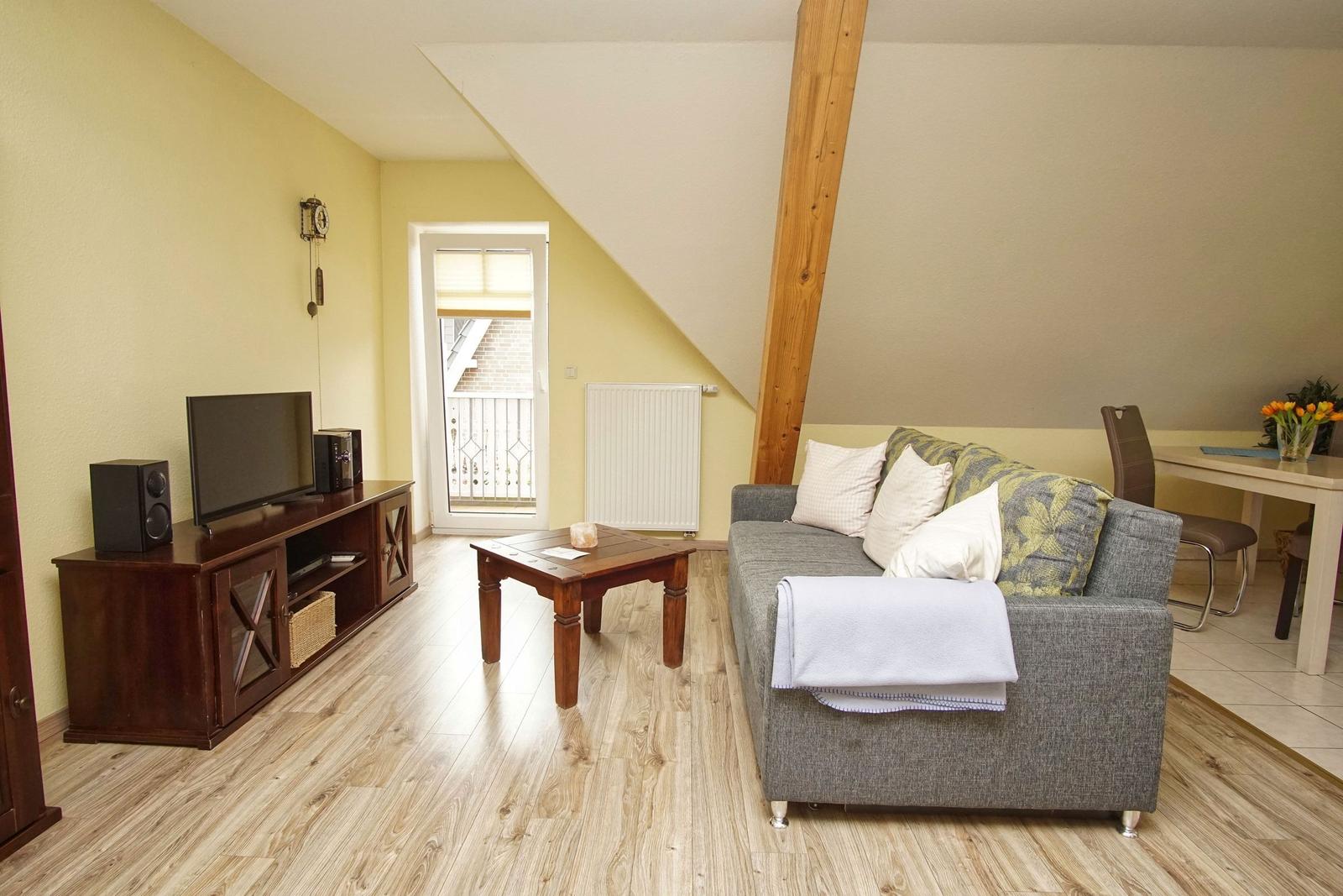 Wohnzimmer mit Sofa, Couchtisch und Fernseher. Holzboden und Balkontür.