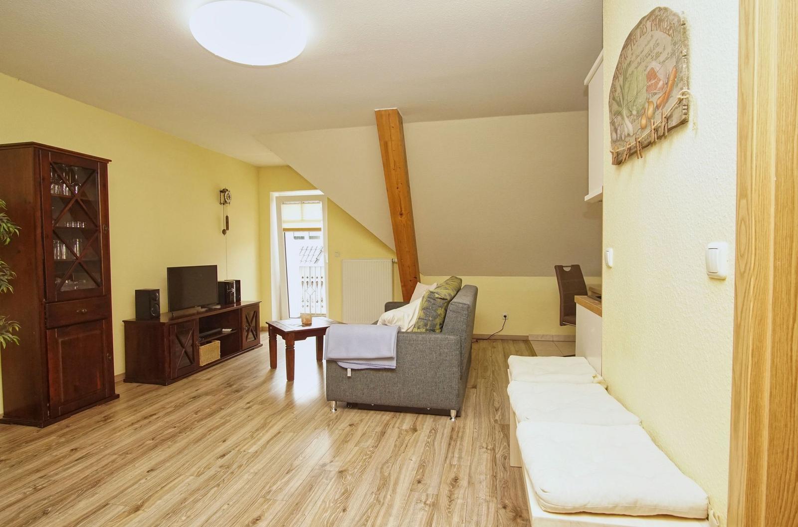 Wohnzimmer mit Sofa, Fernseher und Holzboden. Anbau mit Küchenbereich.