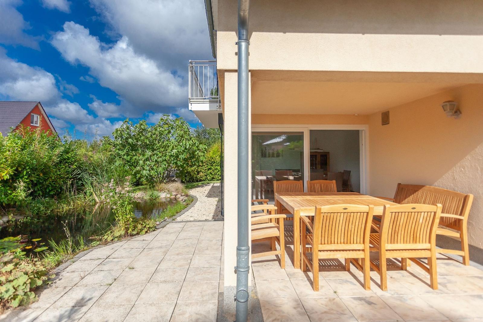 Terrasse mit Holztisch und Stühlen, Blick auf einen Teich und Garten.