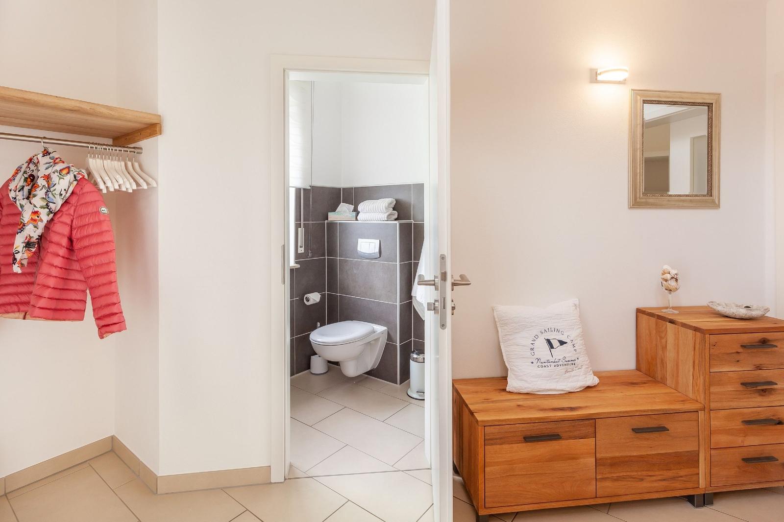 Schlafzimmer mit Kleiderschrank, Holzkommode und Blick in die Toilette.