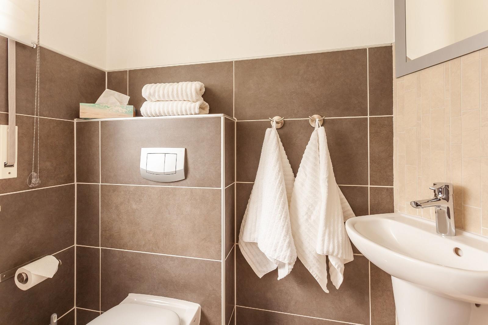 Badezimmer mit Toilette, Waschbecken und Handtüchern.