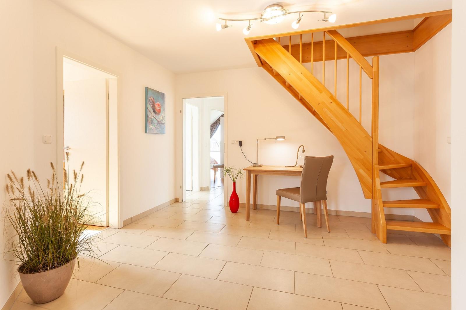 Eingangsbereich mit Holztreppe, Schreibtisch und Pflanzen.
