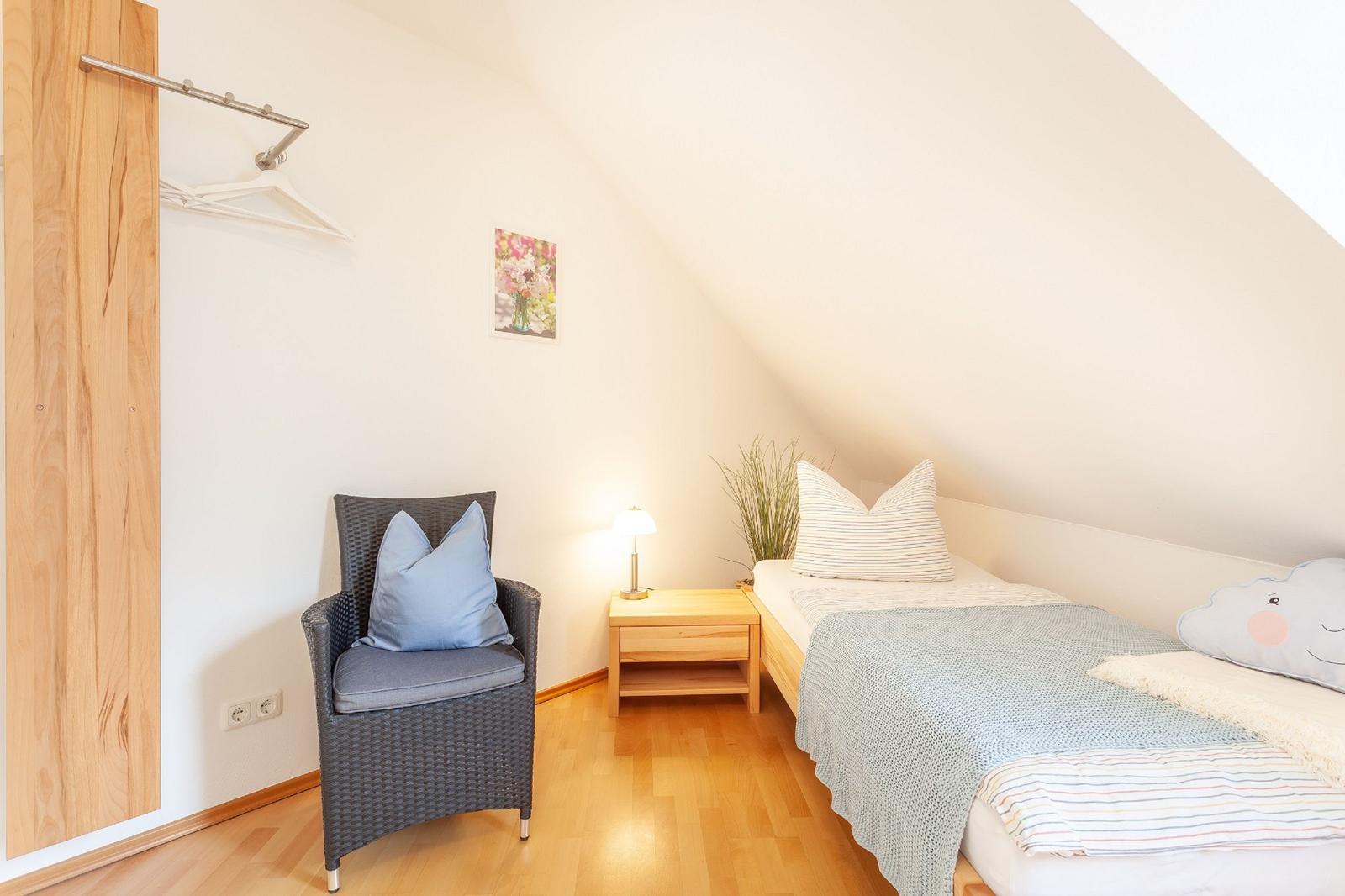 Ein Schlafzimmer mit Dachschrägen, Bett, Nachttisch, Stuhl und Kleiderständer.