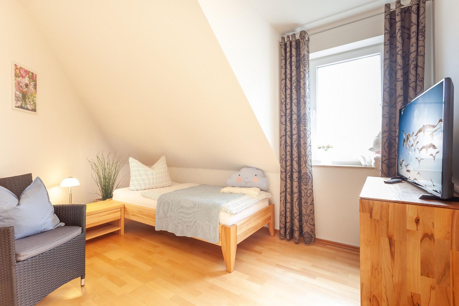 Ein Schlafzimmer mit Dachschrägen, Bett, TV und Fenster mit Vorhängen.