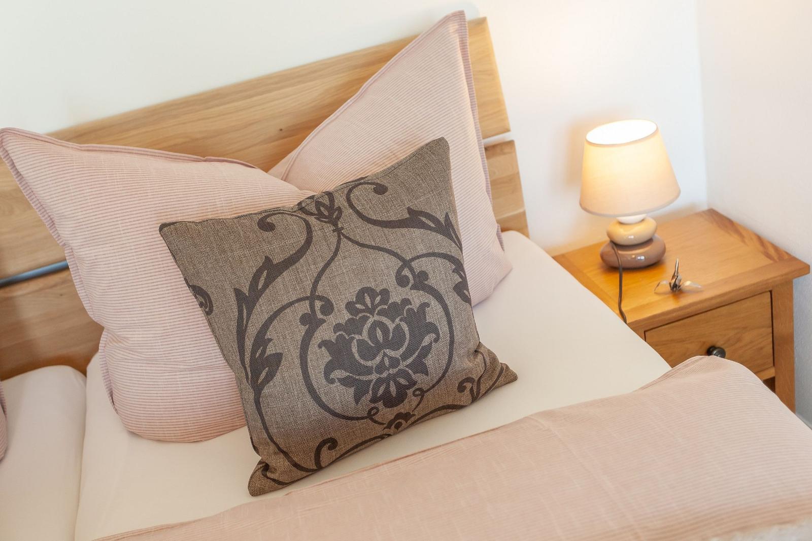 Bettkopfteil aus Holz, Kissen und Nachttisch mit Lampe.