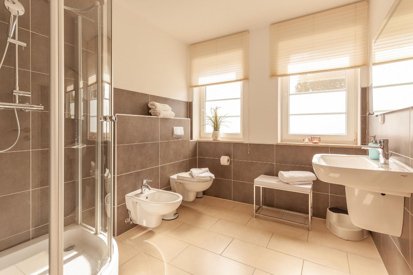 Badezimmer mit Dusche, Waschbecken, Toilette und Fenstern.