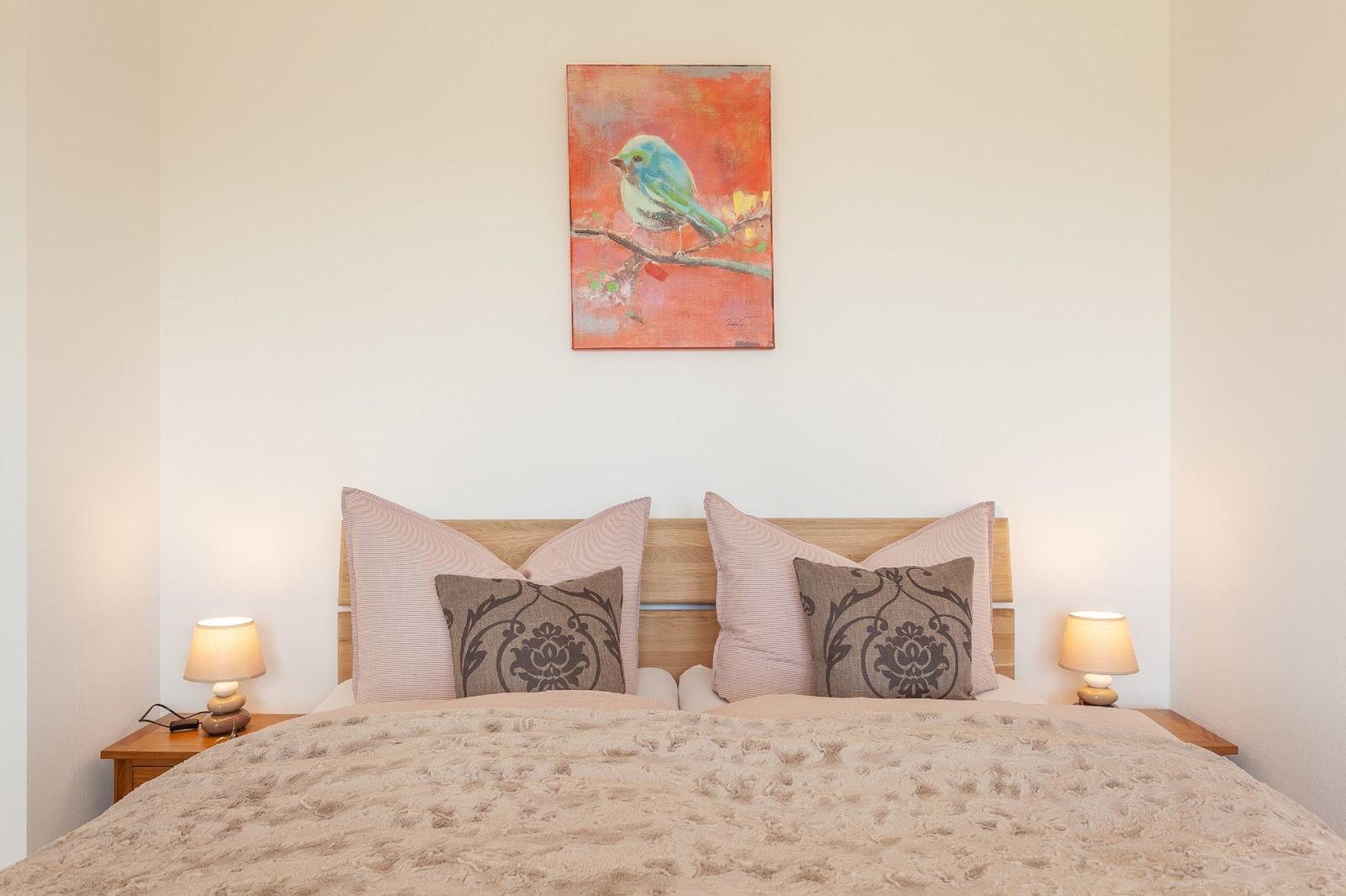 Ein Bett mit Kissen und Decke. An der Wand hängt ein Bild mit einem Vogel.