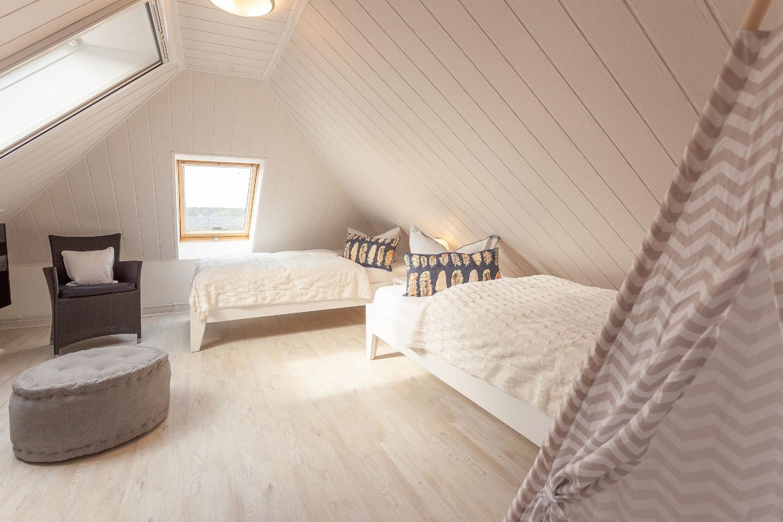 Zwei Betten unter Dachschrägen mit Fenster und Sitzgelegenheit.