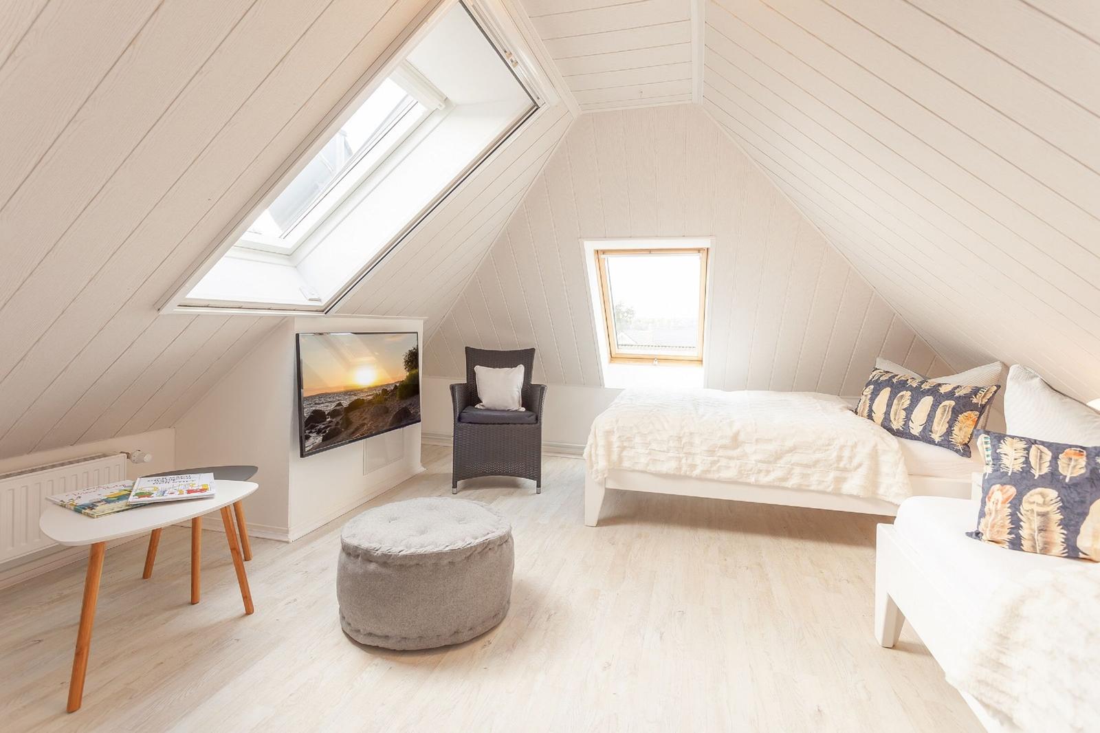 Dachgeschosszimmer mit Bett, Sessel, TV und Dachfenster.