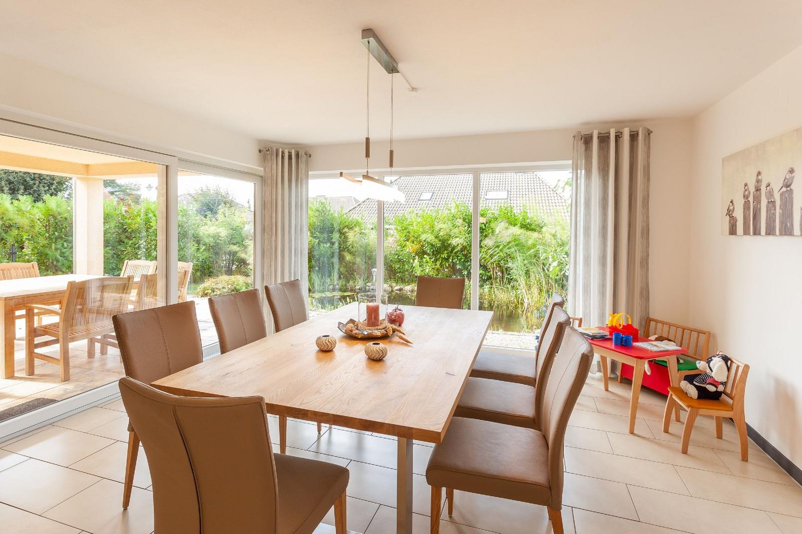 Esszimmer mit Holztisch, Stühlen und Blick auf Garten. Kindertisch und -stühle sind vorhanden.