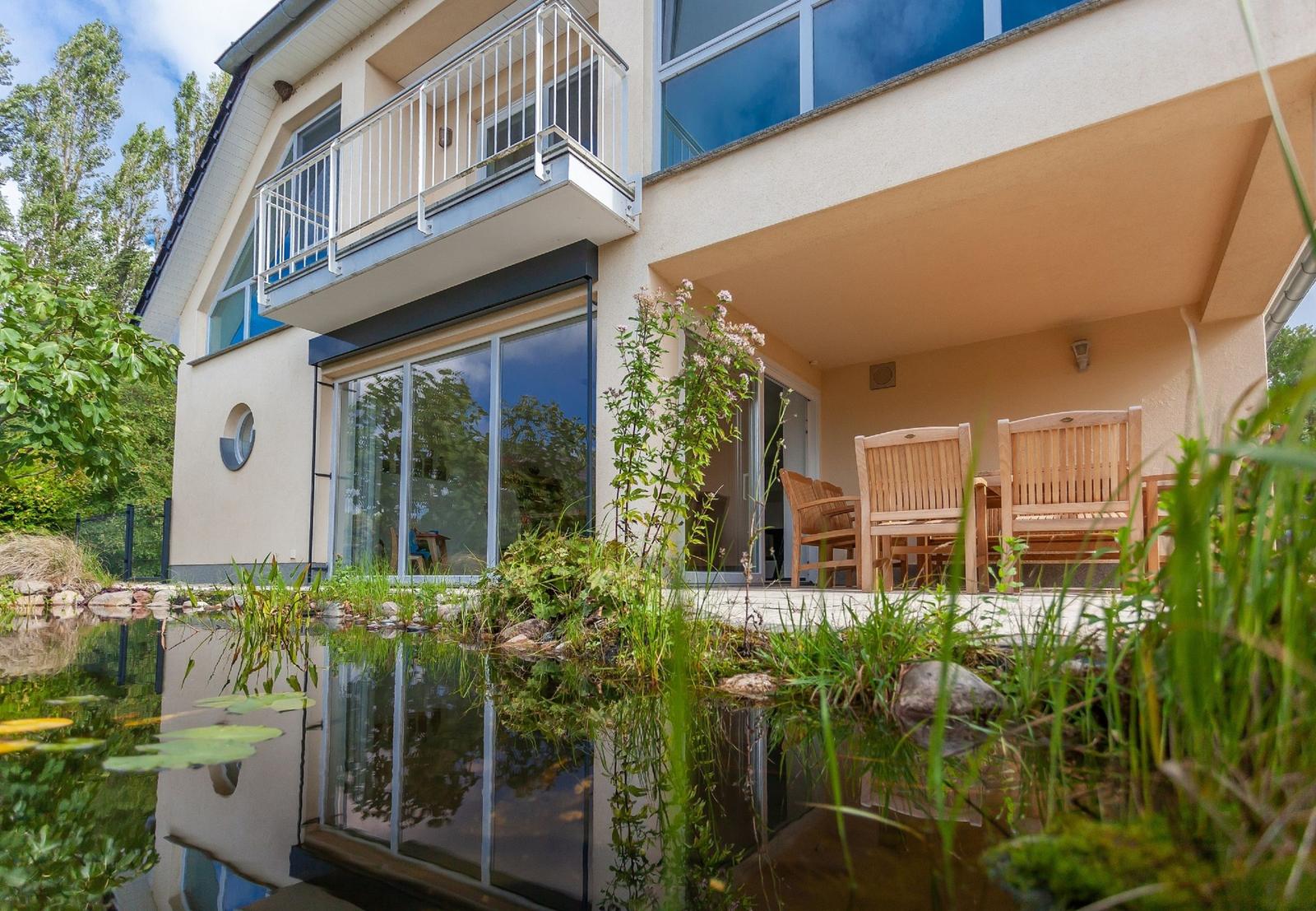 Haus mit Balkon, Terrasse und Teich im Vordergrund.