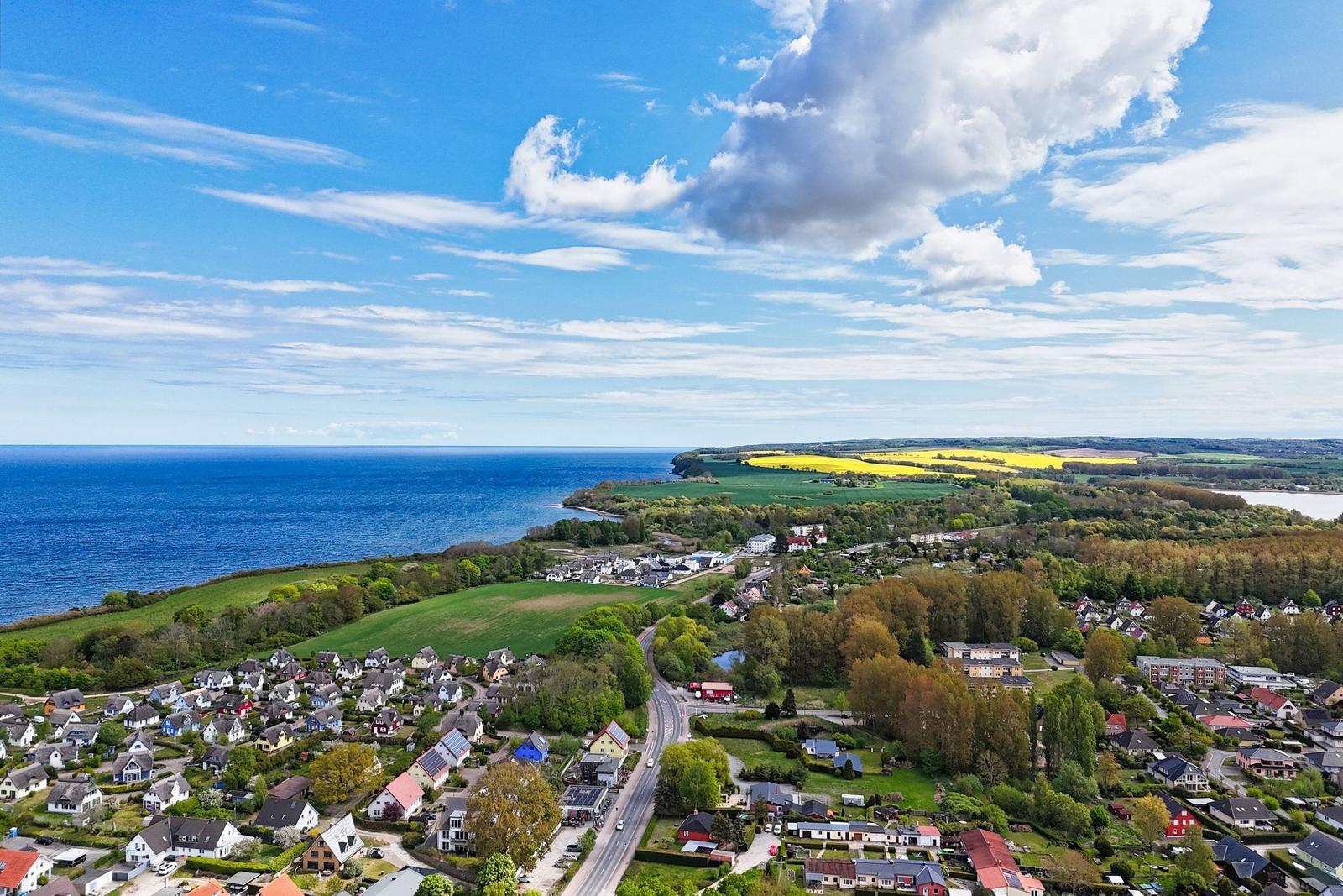 Panoramablick auf Küstenstadt mit grünen Feldern und blauem Meer unter strahlendem Himmel.