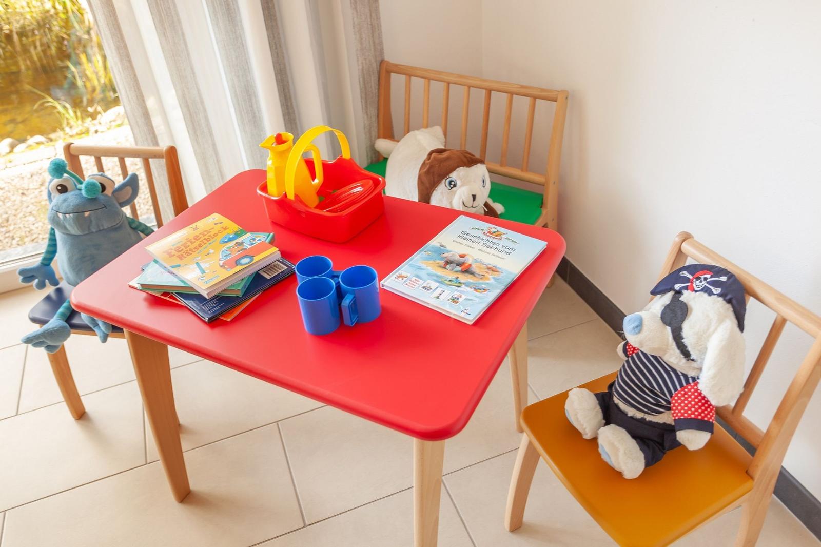 Rotes Kindertisch mit Stühlen, Spielzeug und Büchern. Fenster mit Blick auf Garten.