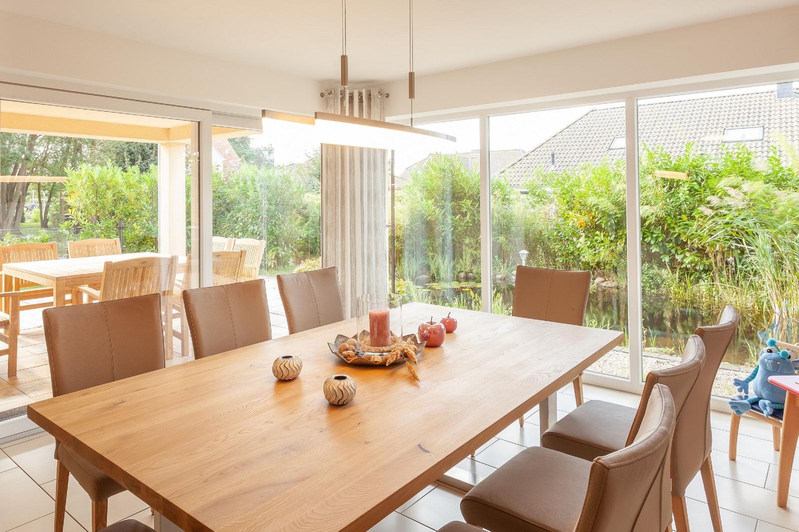 Essbereich mit Holztisch und braunen Stühlen, großes Fenster zur Terrasse und Garten.