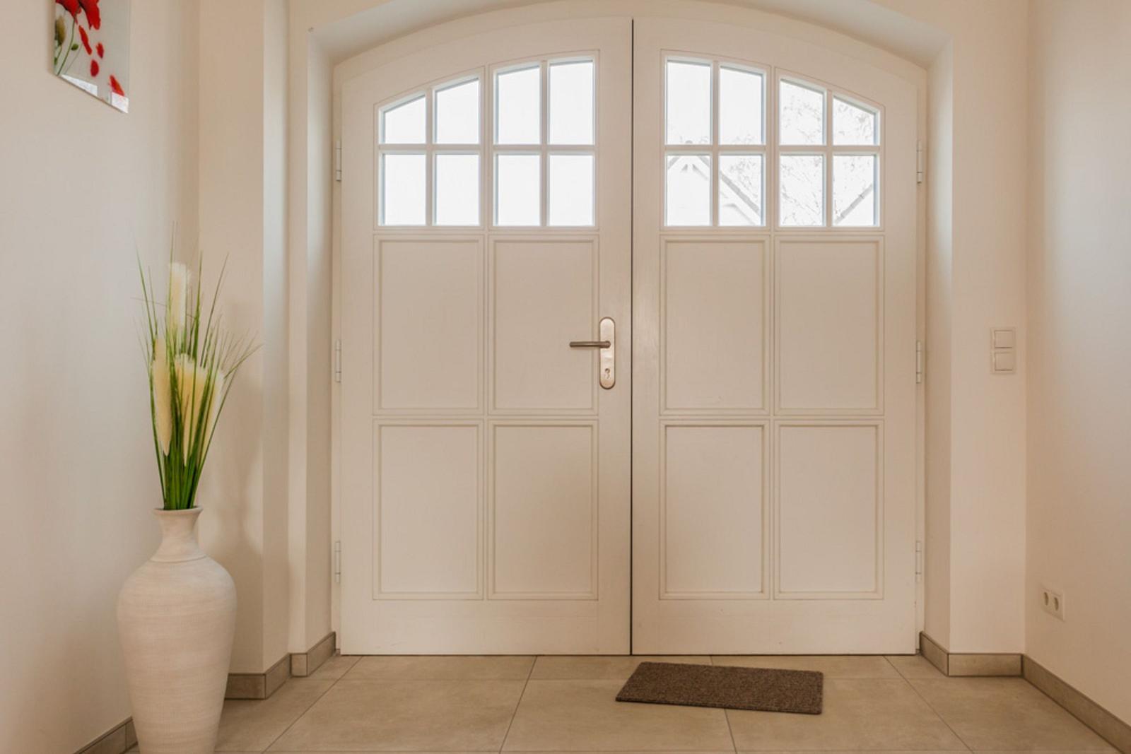 Haus-Eingang mit weißen Doppeltüren und einem weißen Vase mit Pflanzen.