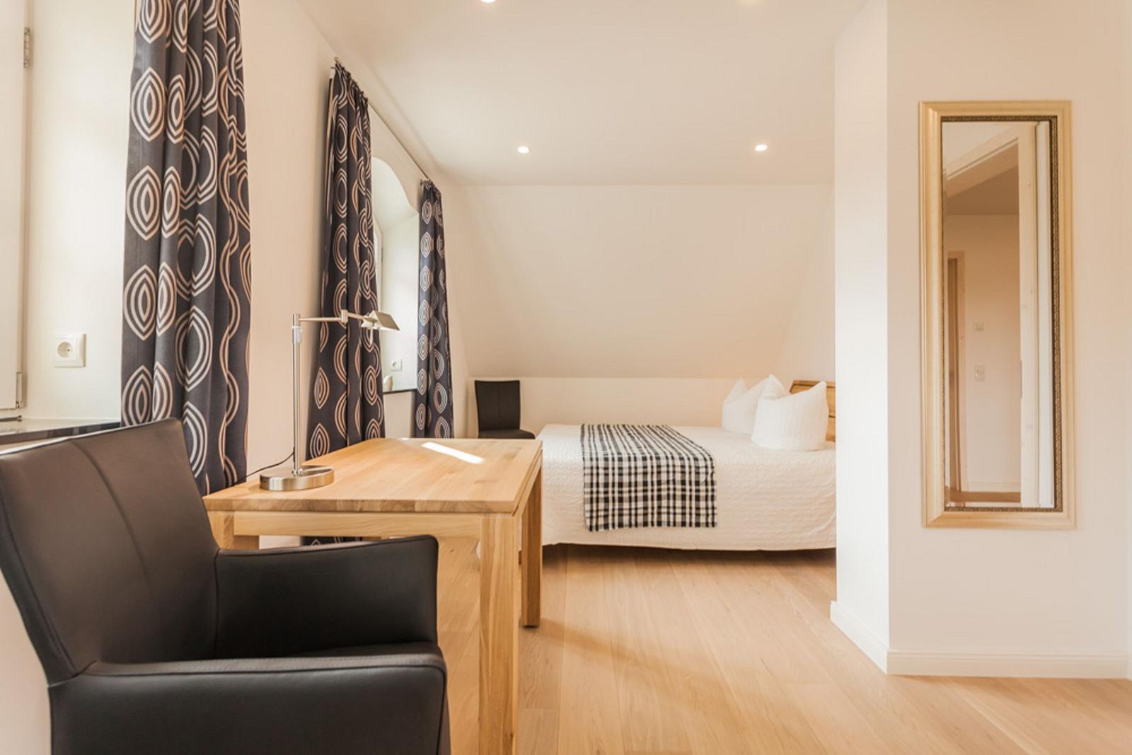 Schlafzimmer mit Bett, Schreibtisch und Spiegel.
