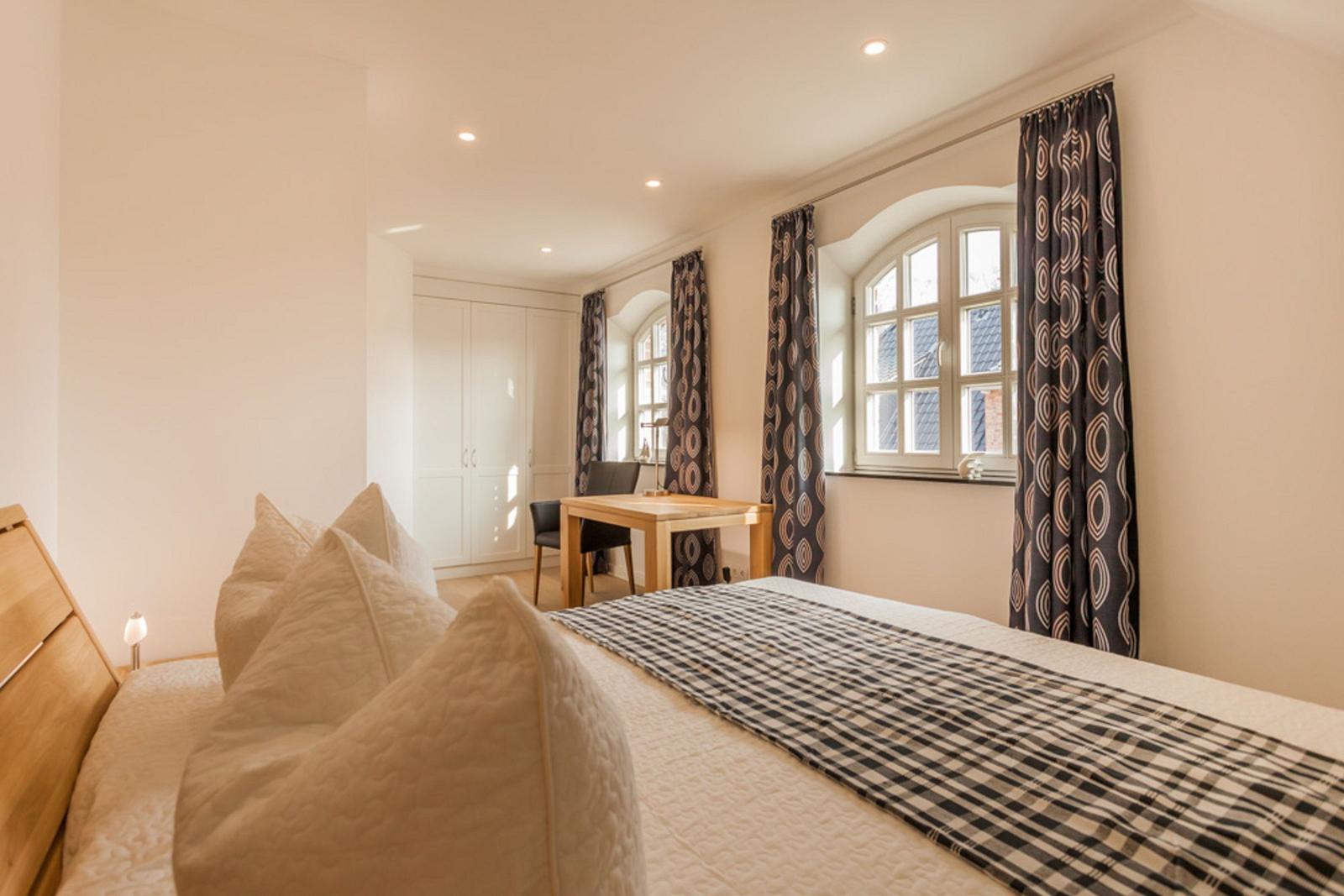 Schlafzimmer mit Bett, Schreibtisch und Fenster mit Vorhängen.